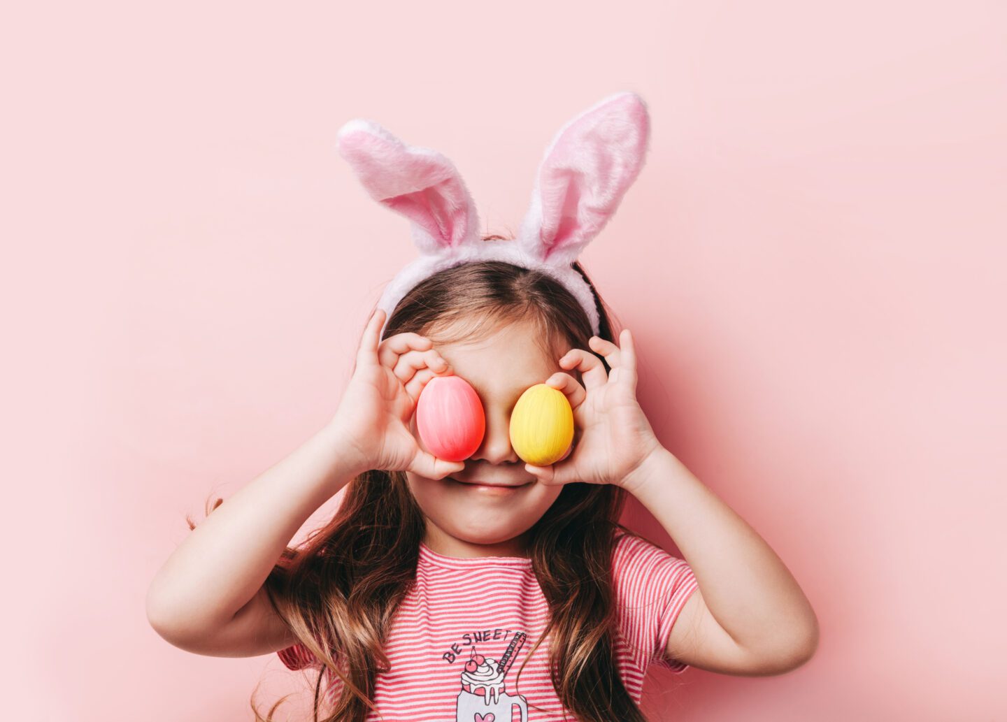 girl wearing Easter bunny ears and holding two eggs, showing her Easter Traditions 
