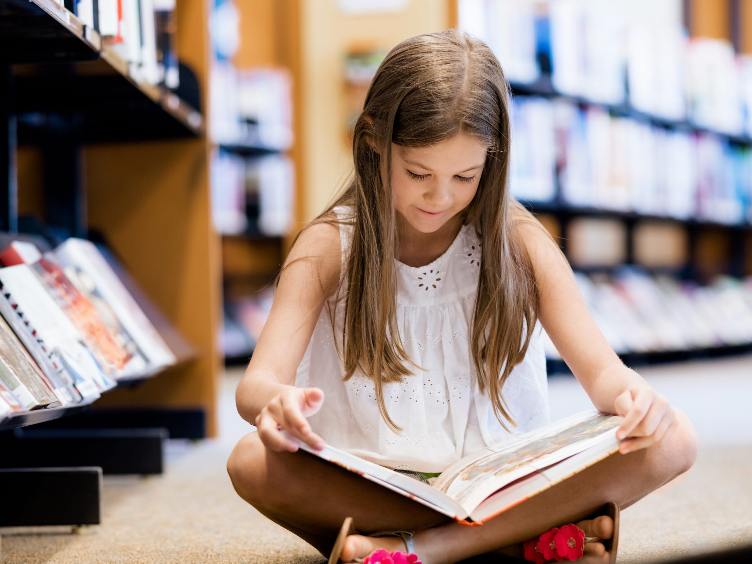 Little girl sitting on the floor crossed leg reading a book for her 4 plus assessment
