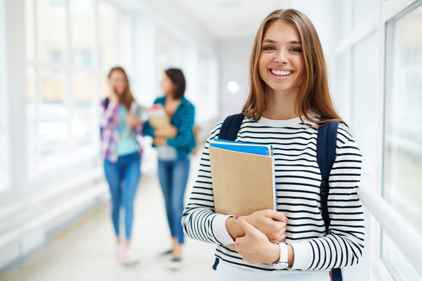 A Level Geography student, wearing a striped long sleeved top holding her books and smiling.